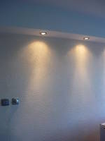 Ściana po remoncie z dwiema lampami punktowymi w suficie, widoczne gniazdka elektryczne poniżej.